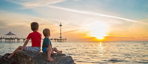 2 kids looking out over the ocean to a sunset